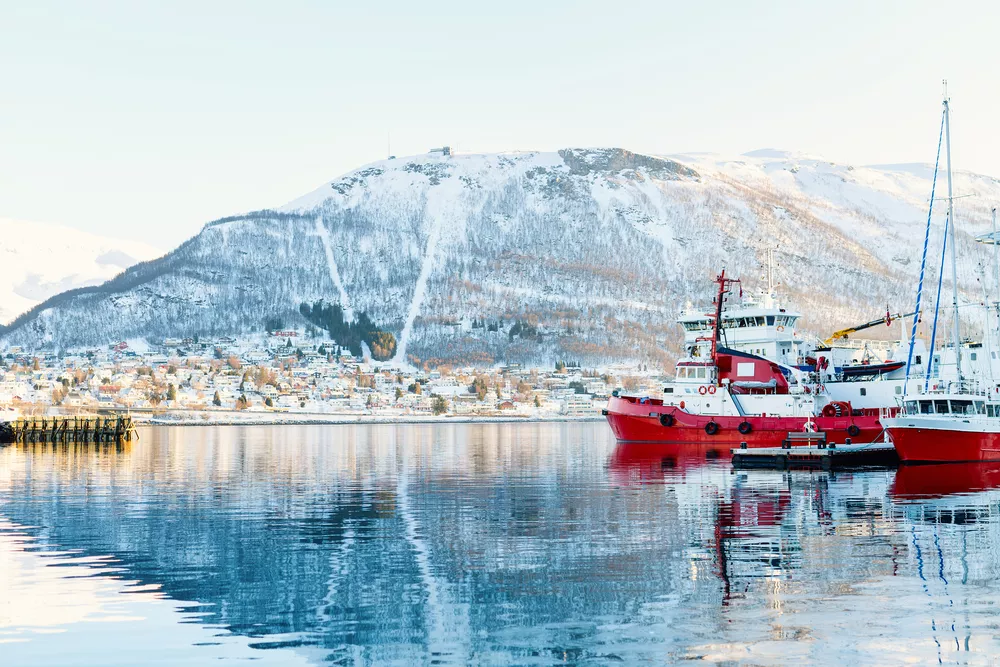 Tromso vanaf de zee, bedekt in sneeuw, terwijl er meerdere boten op het water te zien zijn en bergen op de achtergrond